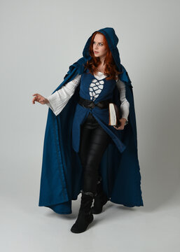 full length portrait of female model wearing medieval fantasy warrior historical costume with blue cloak. silhouette figure,  holding magical spell book on studio background.
