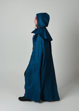 full length portrait of model wearing medieval fantasy warrior historical costume with blue hooded cloak. silhouette figure,  walking away in back view on studio background.