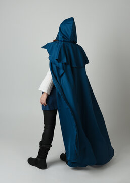 full length portrait of model wearing medieval fantasy warrior historical costume with blue hooded cloak. silhouette figure,  walking away in back view on studio background.