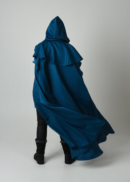 full length portrait of model wearing medieval fantasy warrior historical costume with blue hooded cloak. silhouette figure,  walking away in back view on studio background.