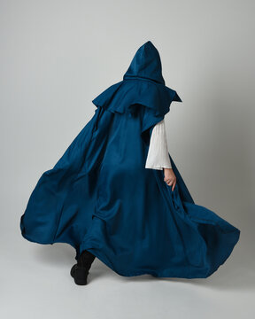 full length portrait of model wearing medieval fantasy warrior historical costume with blue hooded cloak. silhouette figure,  walking away in back view on studio background.