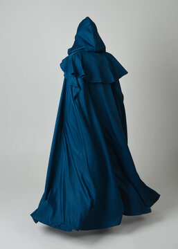full length portrait of model wearing medieval fantasy warrior historical costume with blue hooded cloak. silhouette figure,  walking away in back view on studio background.