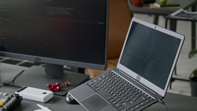 No people medium shot of workstation of software developer or cyber security engineer, with laptop and desktop computer screen displaying lines of code during application testing or database scanning