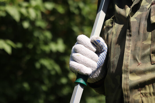 Garden pruner (long-handled pruner), in the hands of a gardener close-up. The tool is designed for pruning high branches and wilted shoots. Hands in gloves with telescopic garden pruners