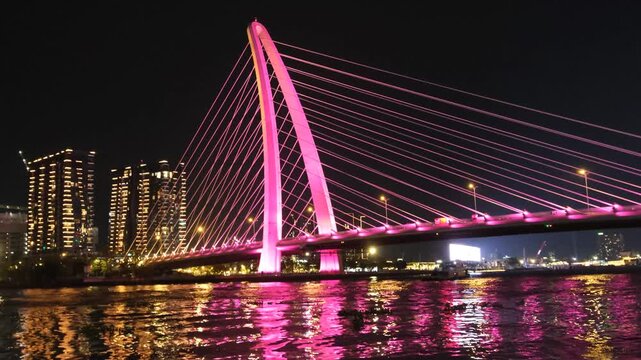 Ba Son Bridge illuminated in pink over the Saigon River at night, with Ho Chi Minh City skyline reflections.