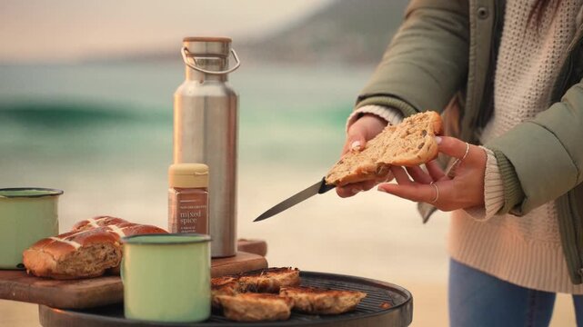 Cutting bread by the seaside, enjoying a serene beachside picnic at sunset