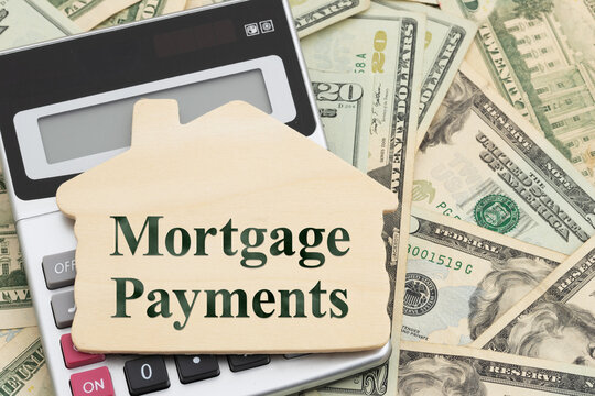 Mortgage Payments text on a wood house with calculator on twenty dollar bills for homeownership costs