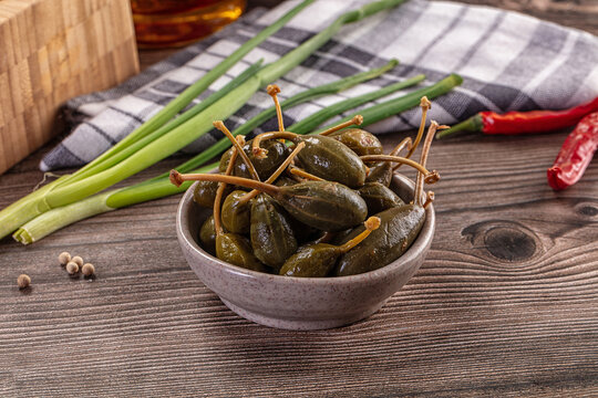Pickled caper berries in a bowl with fresh ingredients on a rustic wooden table.
