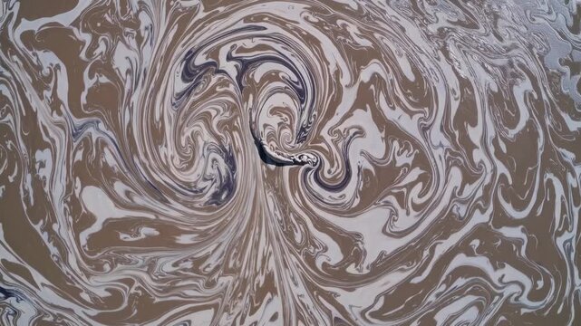 Swirling patterns of brown and white liquid create dynamic motion in a continuous flow, showcasing the mesmerizing transformation of colors and textures in a natural setting