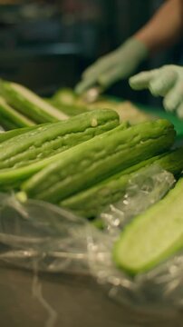 Close-up of Chinese bitter gourd. Woman's hands peeling bitter melon on a board at the market.