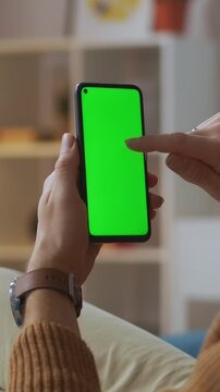 Person using a modern smartphone with a green screen display showing finger tapping and interaction in a cozy indoor environment focused on handheld technology usage