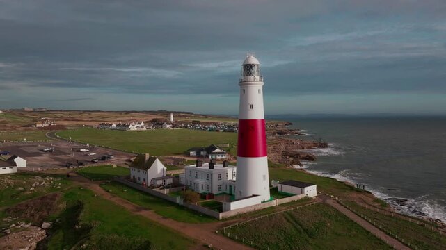 Circular aerial drone panorama of Portland Bill Lighthouse on Portland, Dorset with sunshine against a dark, moody background.