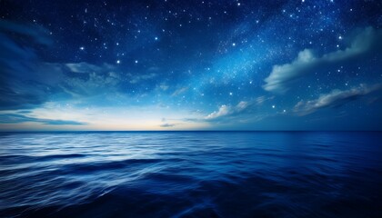 Fototapeta premium A Deep Blue Night Sky Filled With Stars And Clouds Illuminates The Dark Ocean Water Creating An Abstract Heaven Of Light And Space Over The Calm Sea