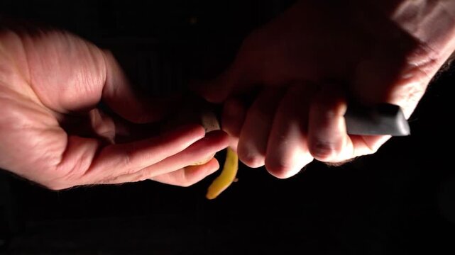 Peeling potatoes with a knife on a black background, peeling vegetables, potato peel