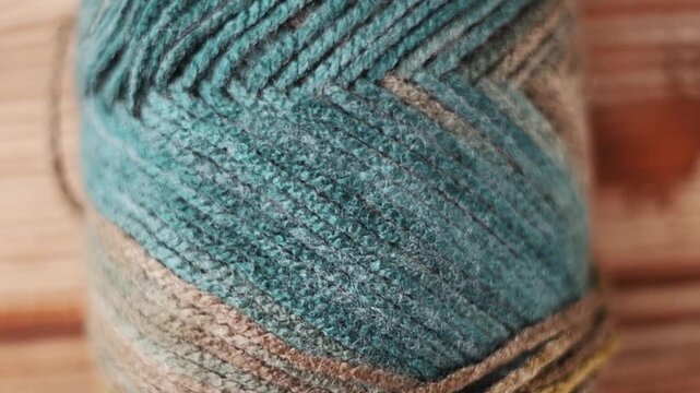 Slow upward pan over a multi-colored yarn skein. Close-up detail of teal, brown, and yellow wool threads on rustic wood. Ideal crafting background.