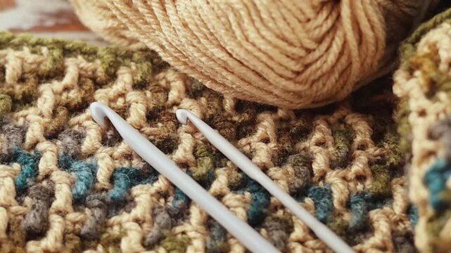 Close-up pan of colorful yarn balls, a crochet hook, and a textured mosaic crochet swatch on a rustic wooden surface. Perfect for crafting backgrounds.