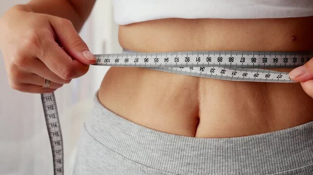 Woman measuring waist with tape measure for fitness and weight loss progress.