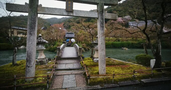 Rain falling over stone torii gate, bridge and stream in ancient Japanese village - steady cam movement