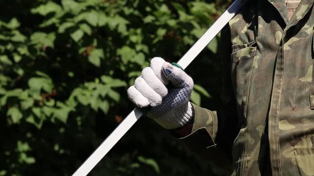 Garden pruner (long-handled pruner), in the hands of a gardener close-up. The tool is designed for pruning high branches and wilted shoots. Hands in gloves with telescopic garden pruners