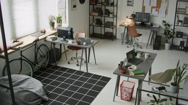 No people overhead security camera shot of software company office with employee desks, computers with code, bicycle by wall and recreational area with bin bag chair and black checked carpet