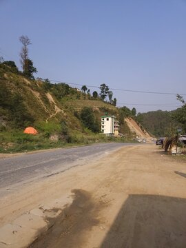 Scenic mountain highway passing through hilly terrain with vehicles traveling along a dusty road construction section.