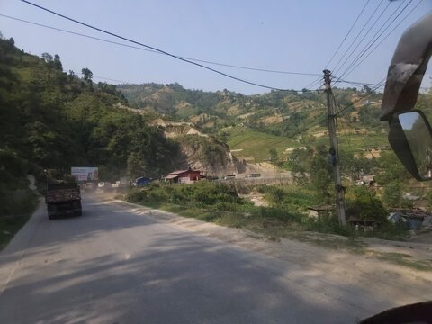 Scenic mountain highway passing through hilly terrain with vehicles traveling along a dusty road construction section.