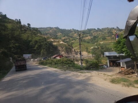Scenic mountain highway passing through hilly terrain with vehicles traveling along a dusty road construction section.