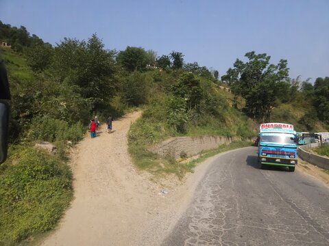 Scenic mountain highway passing through hilly terrain with vehicles traveling along a dusty road construction section.