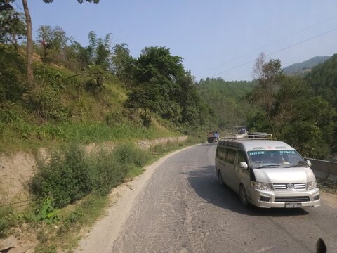 Scenic mountain highway passing through hilly terrain with vehicles traveling along a dusty road construction section.