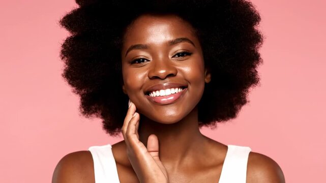 A smiling woman with natural hair touches her face, pink background