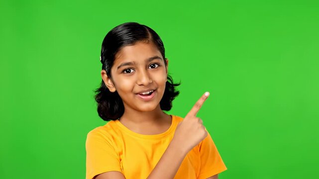 A smiling young girl in a yellow shirt with a green background is clenching her fist