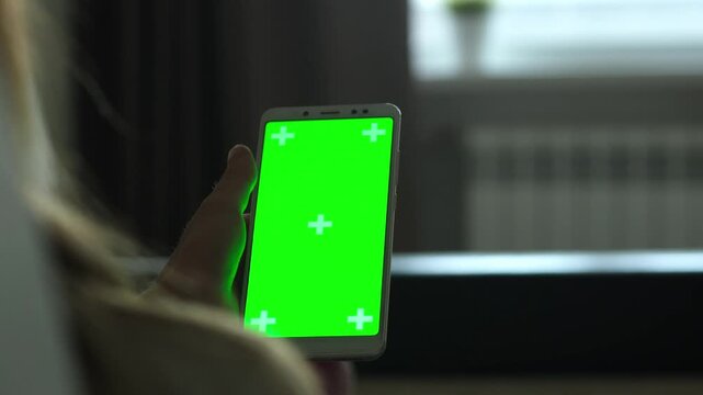 Hand holding smartphone with green screen chroma key in dark room. Mobile app, technology and copy space