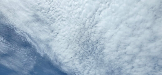 Small, white clouds arranged in wavy patterns resembling fish scales or fluffy sheep's wool fill the sky. Cirrocumulus clouds, also known as "fish scale clouds," are similar to altocumulus clouds   © Vanchuree