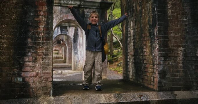 Excited little boy with backpack standing in old arch under bridge in Japan - steady cam shot