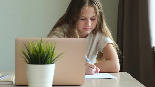 Schoolgirl doing homework with laptop and notebook at home. Concept of distance learning and modern technology in education
