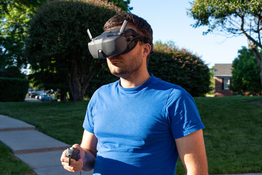 Horizontal photo of a man wearing FPV goggles and holding a mini drone controller, capturing an immersive first-person drone piloting experience and modern aerial technology in action
