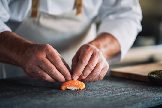A chef's hands carefully arranging a piece of salmon sushi on a dark surface, culinary art