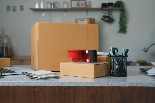 Entrepreneur home office workspace featuring cardboard parcel boxes laptop and packing supplies during e-commerce business shipping operations