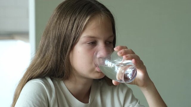 Girl drinking clean transparent water from glass at home. Healthy body care
