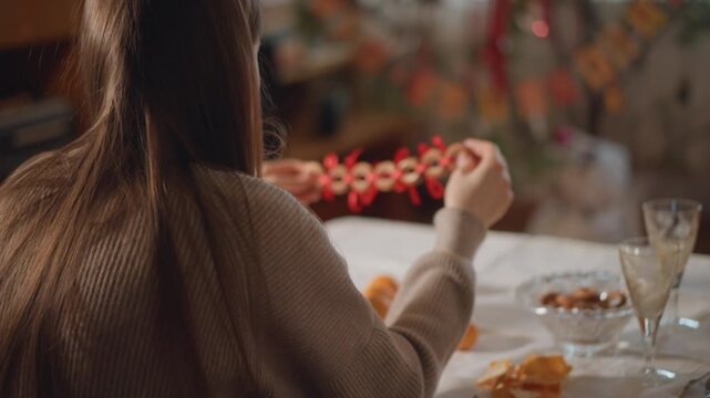 Young woman decorates with berries at craft table. Artist handcrafting red berry garland in cozy studio space. Female creator assembling red berry garland during intimate craft session at home