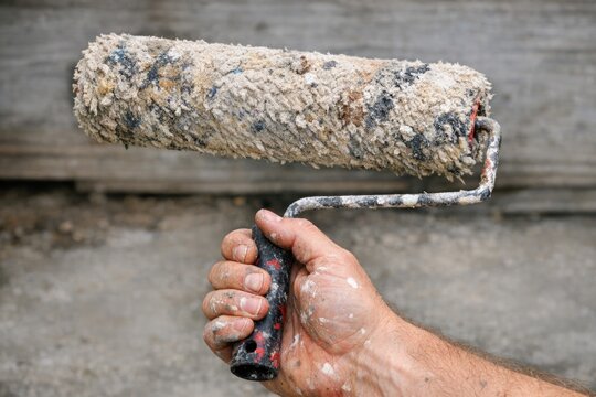 A person holds a paint roller with a matching brush, ready to start painting
