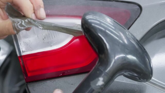 Skilled worker in a detailing shop carefully removing a protective tint film to a modern car's rear light, using a heat gun and squeegee for a precise and bubble-free installation