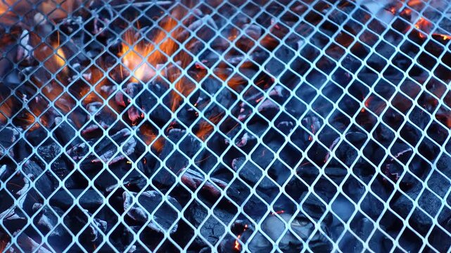 Metal bbq grill grate with burning charcoal, fire flames, and smoke blurred in the background