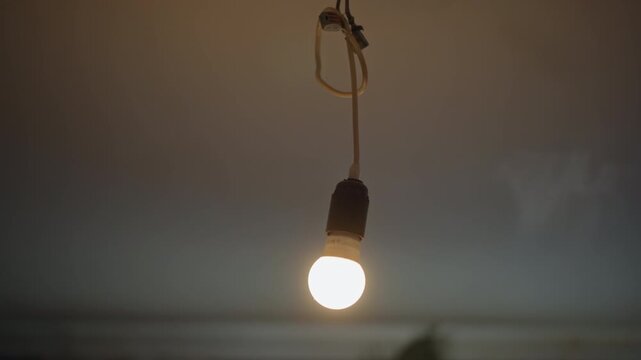 Single dangling bulb casting warm glow, shallow depth of field with bokeh, soft pool of light on interior surface, visible cord loop at ceiling, minimalist evening mood, calm domestic scene