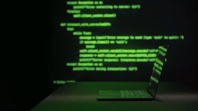 Laptop with hacking software on table in dark room, green code lines moving in background. Cyber attack, malware activity, data breach and cybersecurity threat concept. Copy space