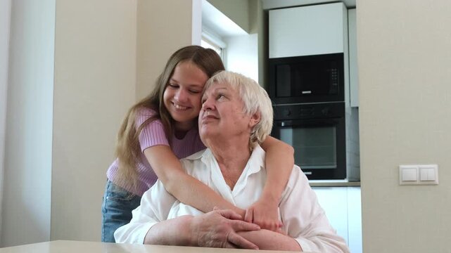 Smiling teen girl hugging and kissing her grandmother at home. Granddaughter with granny