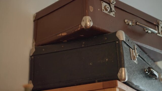 Stacked vintage cases on wooden cabinet in loft studio, artist using suitcases as props for still life scene, warm natural light, textured leather and metal corners adding retro ambiance.