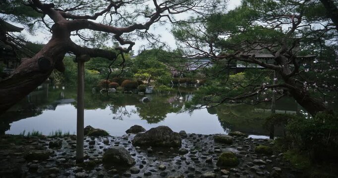 Beautiful, reflective pond near rocky shore and with surrounding trees in Japan - wide shot