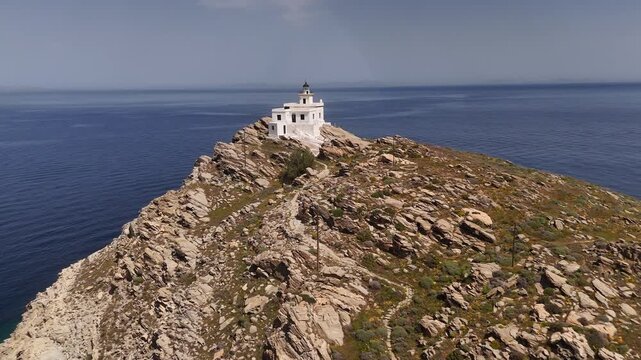 4K drone approach and centered 360 orbit rotation of Korakas Lighthouse on rocky cliffs, Paros, Greece