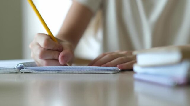 Hand of schoolgirl writing close up. Kid doing homework at home. Little student studying indoors. Education and back to school concept